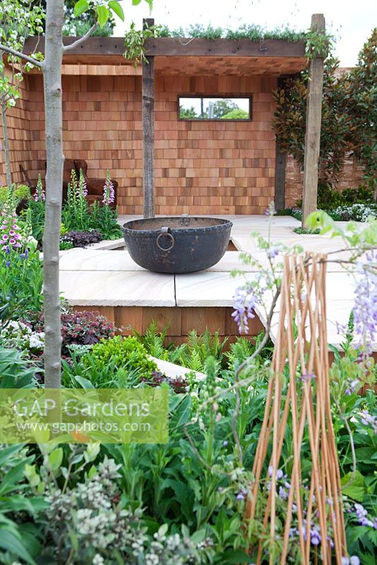 Large cauldron copper pot on sandstone paving, plants in foreground.