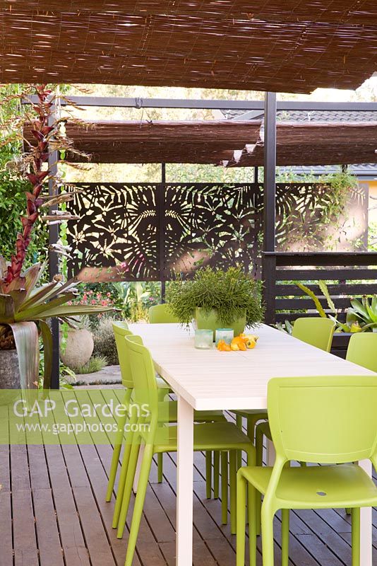 Timber deck with informal dining area and decorative timber screen in background. Table with potted rhipsalis. Potted Alcantarea seen at left