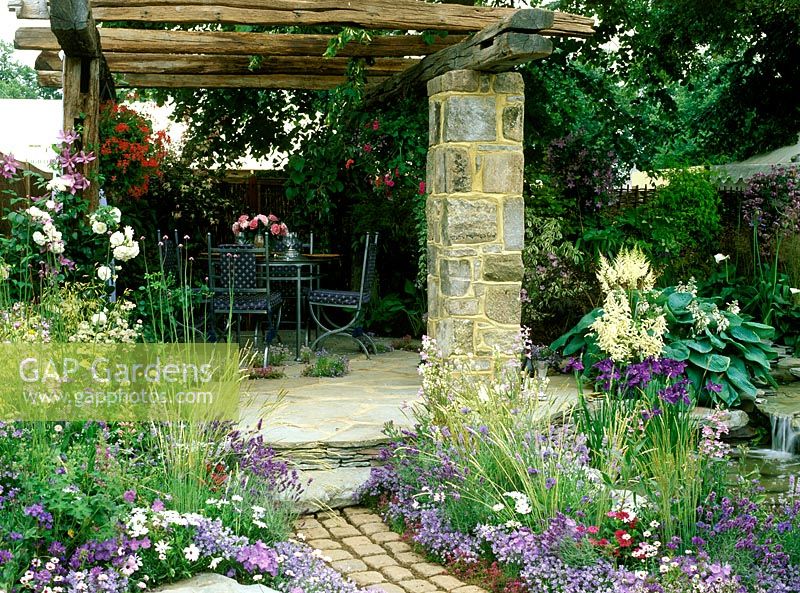 Patio with furniture, Hampton Court 2001, Design: Paul Dyer, the sound of the countryside. Crazy paving patio with table and chairs, old timber pergola, geranium hanging basket, clematis, rosa and verbena bonariensis