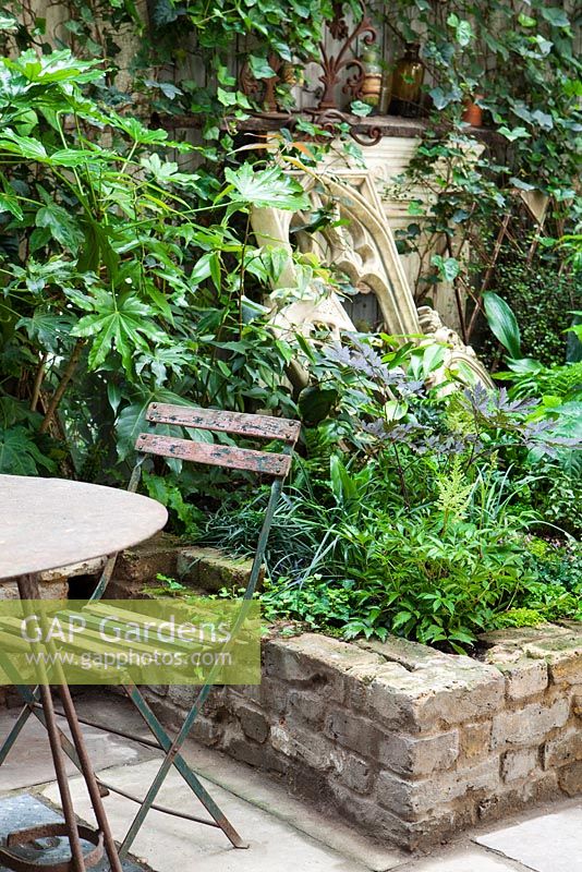 View of raised wall beds with table and chair, church feature and old fire place, Lucille Lewins, small court yard garden in Chiltern street studios, London. Designed by Adam Woolcott and Jonathan Smith 