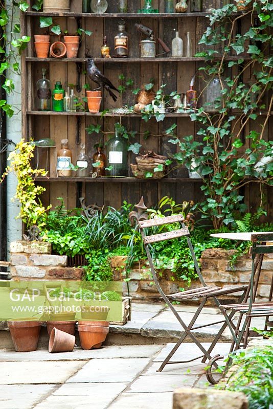 View of court yard with table and chairs to shelves with artefacts. Lucille Lewins, small office court yard garden in Chiltern street studios, London. Designed by Adam Woolcott and Jonathan Smith