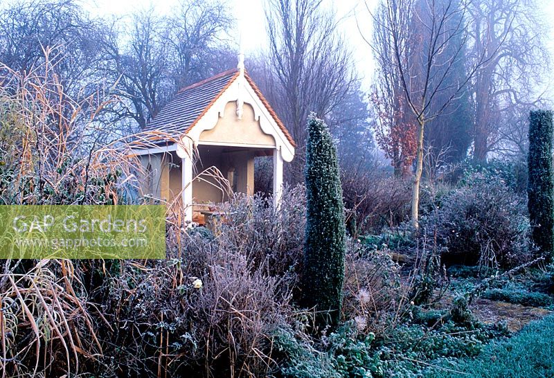 Garden in winter with hoar frost. Borders with garden building summerhouse. 