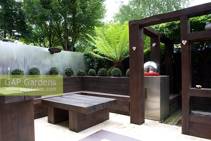 Rail sleeper timber garden divider with ornamental found objects in niches.  Furniture, box balls, raised bed, aluminium fencing. minimalist. 