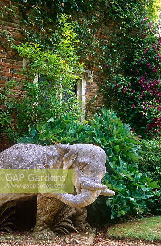 One of a pair of elephants framing the entrance to the South Court with Clematis 'Etoile Violette' climbing the gatehouse behind. Cranborne Manor Garden, Dorset