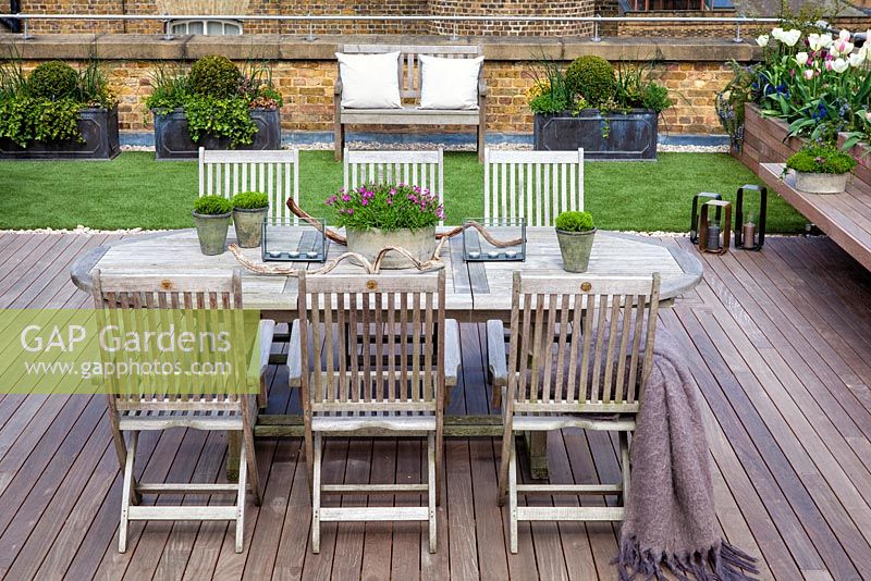 Dining table and chairs with faux lawn on a London roof terrace garden. April. 