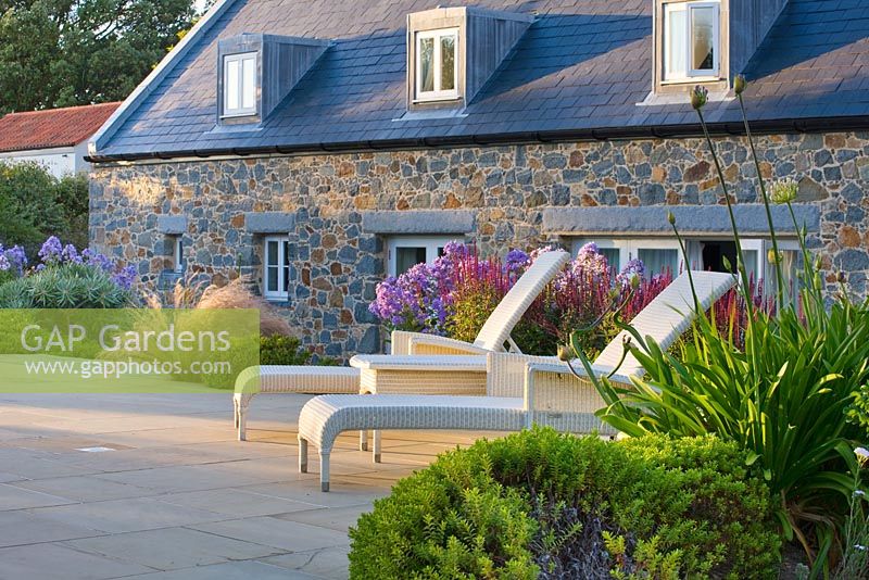 Sunbeds next to stone house.  Planting includes Stipa Tenuissima and Campanula. 