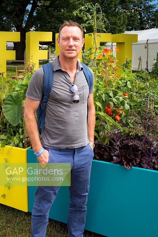 Designer Terry Oliver in front of colourful metal planters full of vegetables. Including nasturtiums, sweet peppers - capsicum, a trailing hop - Humulus lupulus and purple-leaved kale. Designer: Terry Oliver, Sponsor: Royal Borough of Kensington and Chelsea