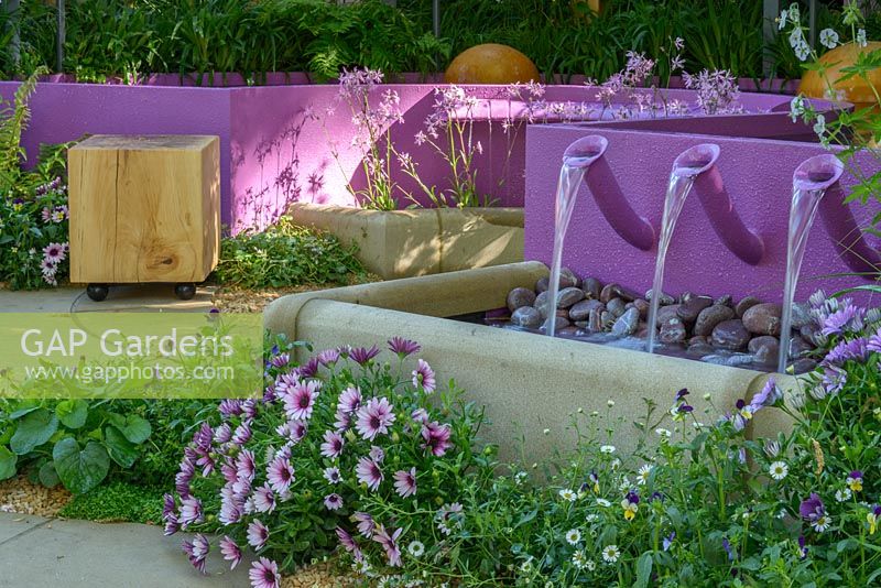 Water cascades from violet pool in Papworth Trust - Together We Can with acustic effects generated by water merimba. RHS Chelsea Flower Show 2016. Sponsor: Papworth Trust. Designer: Peter Eustance MSGD. SILVER GILT