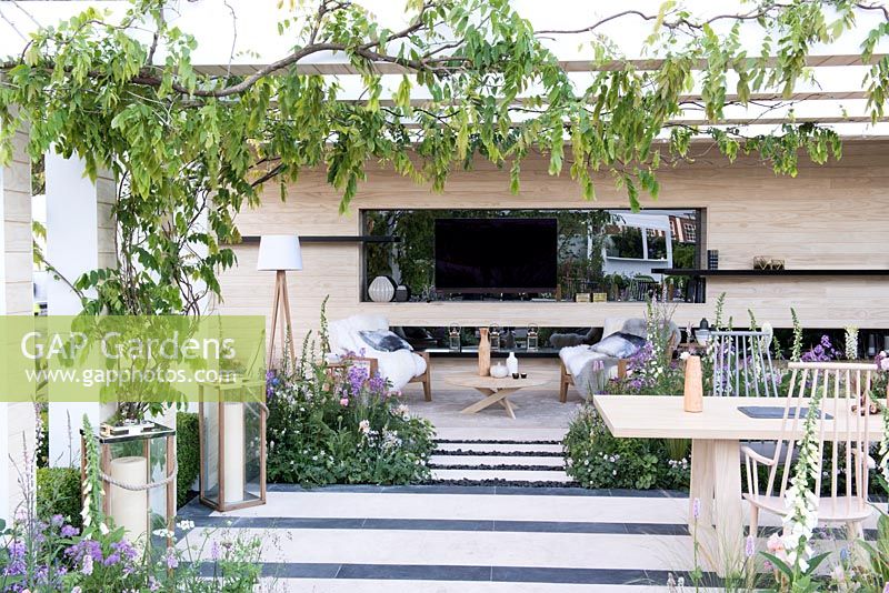 Wisteria 'Schowa Beni' climbing a pergola over a dining area with outdoor tv - The LG Smart Garden, RHS Chelsea Flower Show 2016. Designer: Hay Young Hwang, Sponsors: LG Electronics