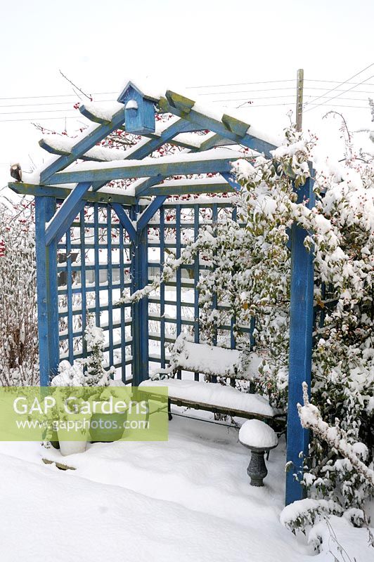 Snow covered garden arbor with garden seat and potted plants, Norfolk, UK, December