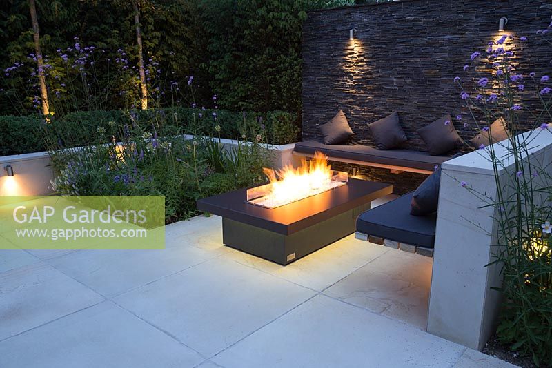 Secluded seating area with a dry stone slate wall and propane fire pit emitting yellow light