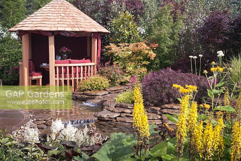 A natural stone edged pond and wooden gazebo. Garden: 'Reflections' at RHS Tatton Park Flower Show 2012