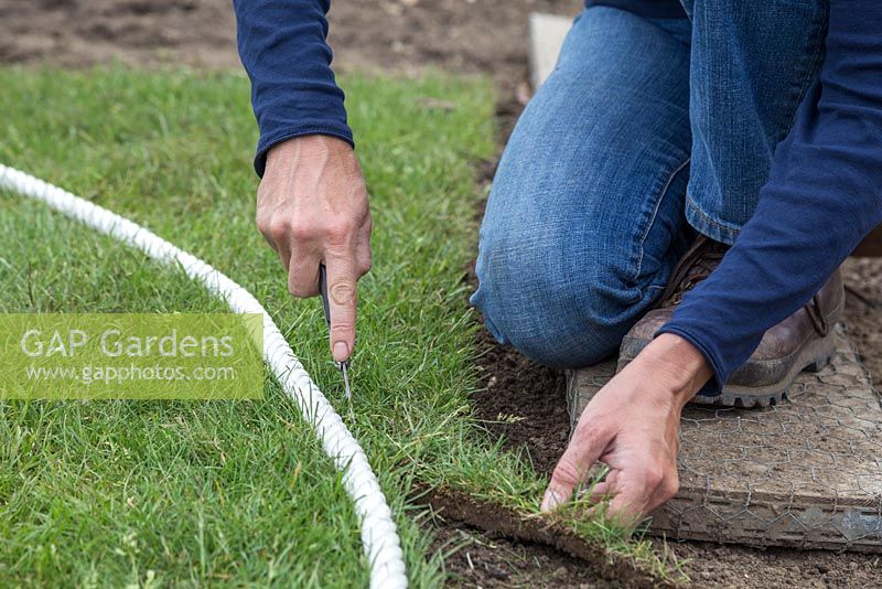 Using a knife to cut newly laid turf to shape, following along the rope guide