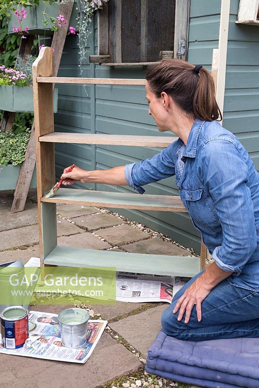 A woman painting book shelves with green paint