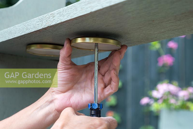 Screwing glass jar lids underneath the book shelf