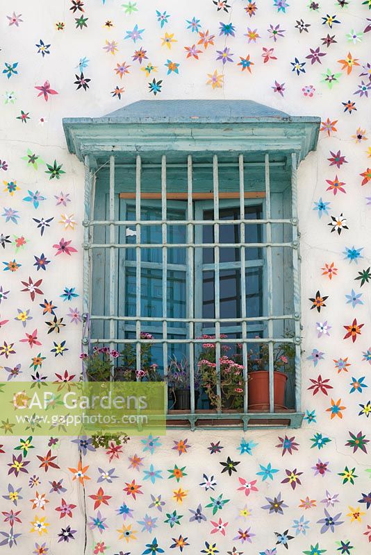 Pale blue painted window surrounded by artificial flowers with grille and pots of pelargoniums, Cordoba, Spain