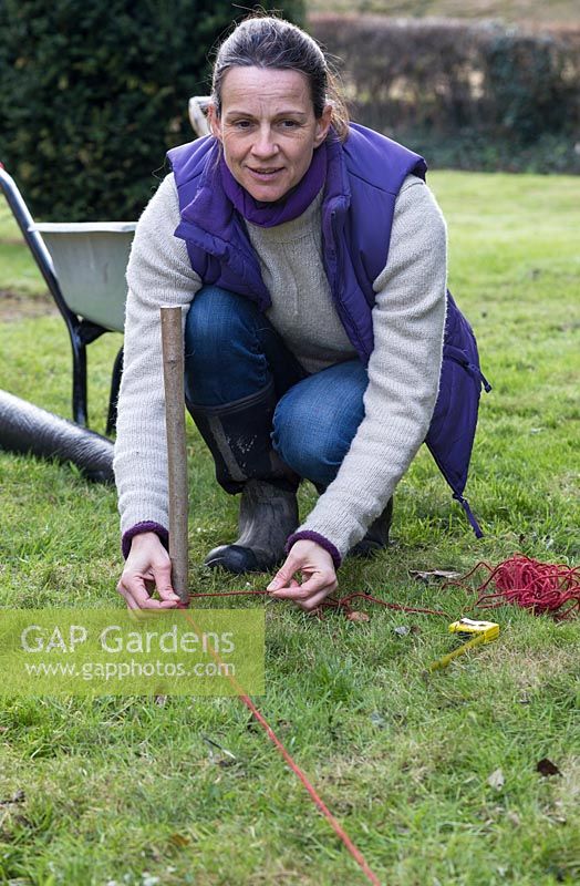 A woman using stakes and string to create a guide outline for the base of the arbour 