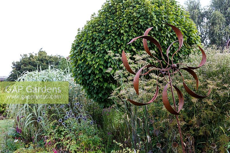 Little Ash Garden, Fenny Bridge, Devon. Autumn garden. Rusted metal 'Windmill' sculpture in autumn border. 