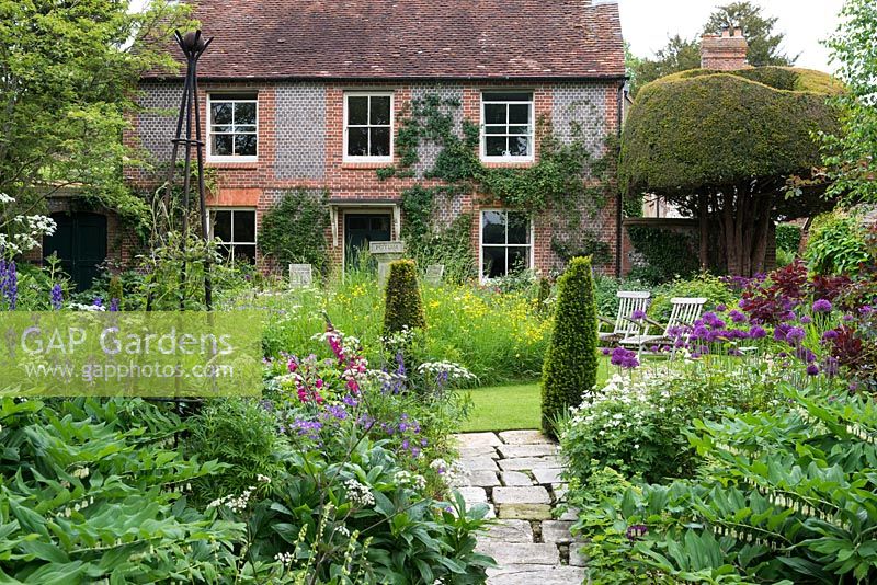 A 19th century cottage with circular lawn, raised wildflower mound, yew topiary and mixed borders with Anthriscus 'Ravenswing', Allium 'Purple Sensation', Geranium sylvaticum 'Album', Polygonatum x hybridum and Gladiolus byzantinus.