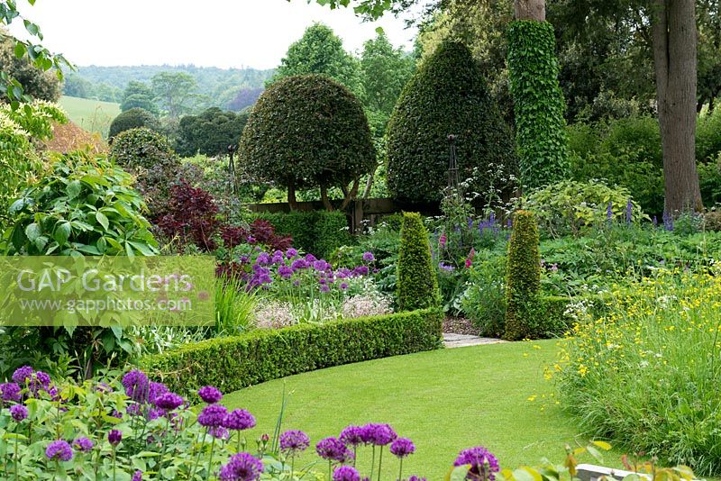 A cottage garden with circular lawn and raised wildflower mound. The formal structure is created by low box hedging, conical shaped yews and domed holly trees.