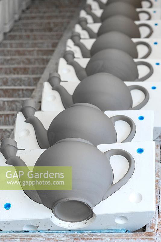 A line of teapots, newly solidified, with one half of the mould removed so they can dry out.