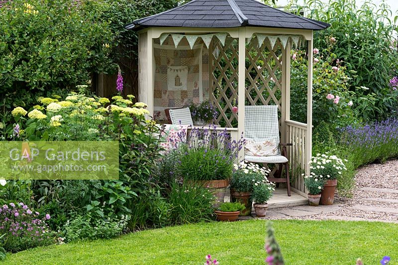 Overlooking the lawn and borders, a gazebo is flanked by pots of lavender and marguerites, Hydrangea arborescens 'Annabelle' and roses.