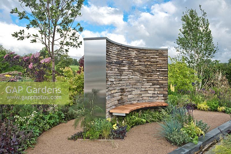 The Cruse Bereavement Care: A Time for Everything garden at RHS Chatsworth Flower Show 2017. Drystone wall with wooden bench seat, water feature rill channel, hardstanding area with island beds of herbaceous perennials, shrubs and treesDesign: Neil Sutcilffe