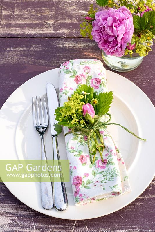 Summer table place setting with pink roses, alpine strawberry flowers and alchemilla mollis