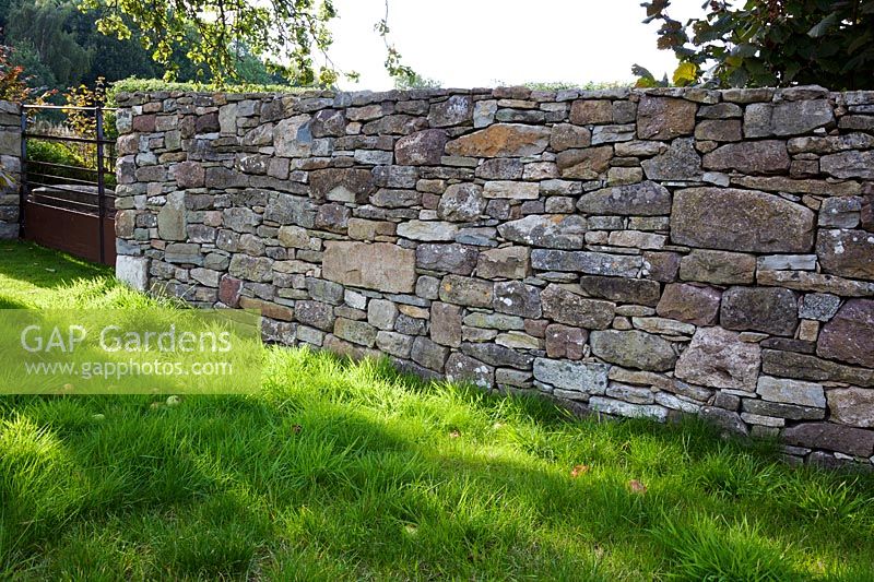 Detail of a drystone boundary wall and rusty iron gate in a country garden
