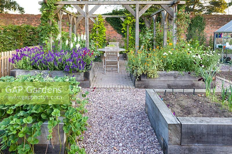 A greenhouse and raised beds for fruit, vegetables and cut flowers in a modern Cheshire country garden. It was designed by Louise Harrison-Holland. Plants include strawberries, Salvia viridis and Antirrhinums.
