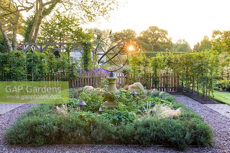 The dawn sun shines through an armillary sphere, which provides a focal point in a modern Cheshire country garden. It was designed by Louise Harrison-Holland, planting includes Stipa tenuissima, lavender and roses.