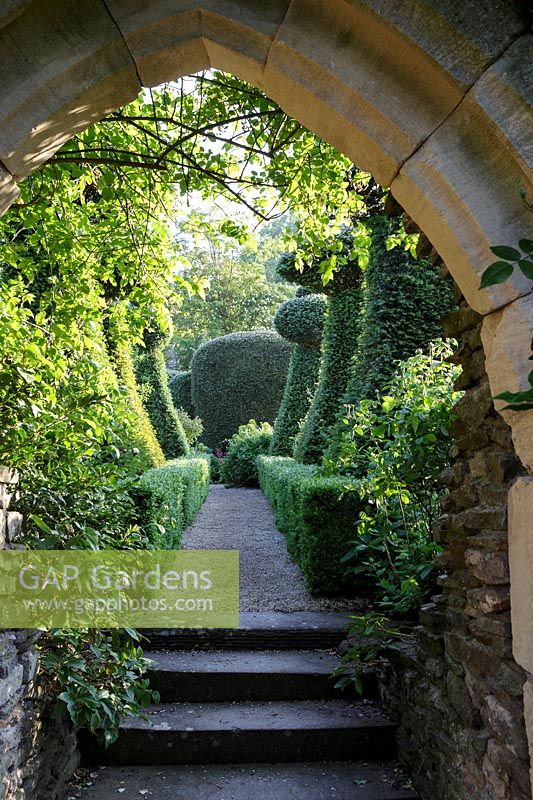 Hanham Court Gardens, Bristol. Early summer garden. Arch leading to topiary avenue