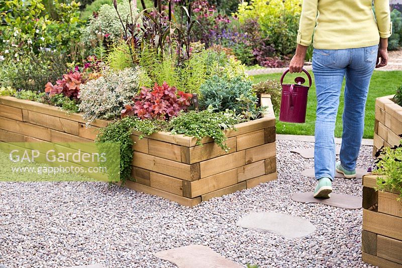 Woman walking away after watering wooden raised bed of Summer plants