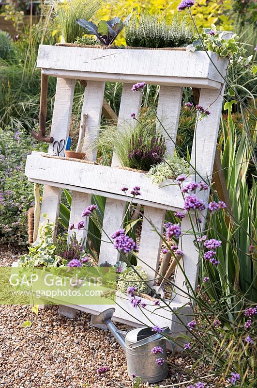 White pallet planter with garden tools and a mix of flowers, grasses and herbs