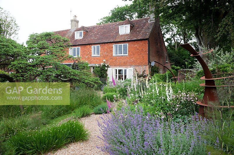 view of the house and borders with old Pear tree in meadow, rusted Corten sculptures, Nepeta 'Tapdance', Nicotiana mutabilis, Digitalis purpurea and purpurea 'Alba'.