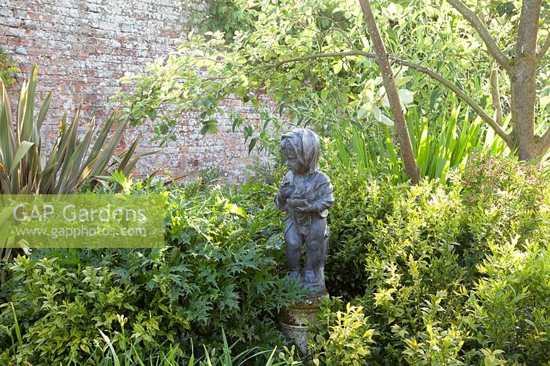 Decorative statue of child amongst mixed foliage for texture in walled garden