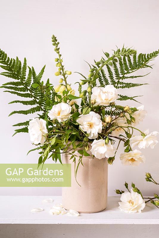 Flower arrangement with white roses, foxgloves, jasmine and ferns in cream jar