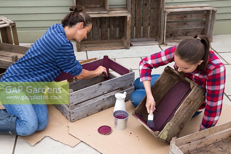 Woman and young girl painting inside of wooden crates