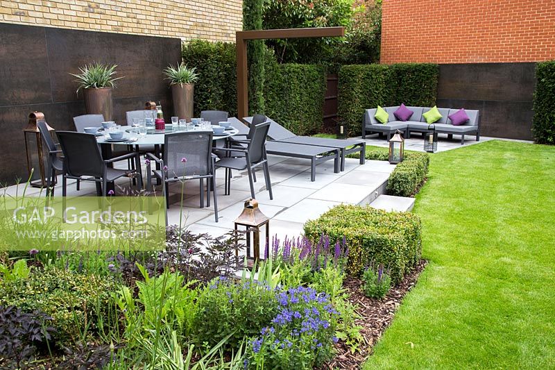 Contemporary suburban garden with copper feature wall, patio with dining furniture and hedging