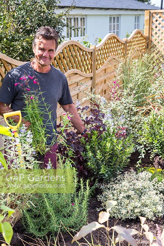 Antony Henn from Garden on a roll by newly planted border of mature plants where plants are placed according to the paper plan for the designed border