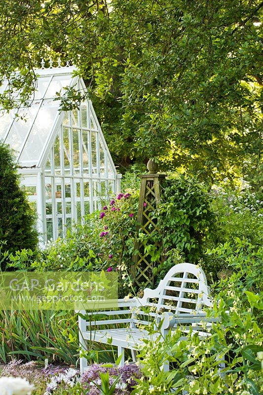 Secluded place with garden bench under a mature English oak, obelisk as support to roses and clematis backed with a conservatory. Design: Carol Bruce