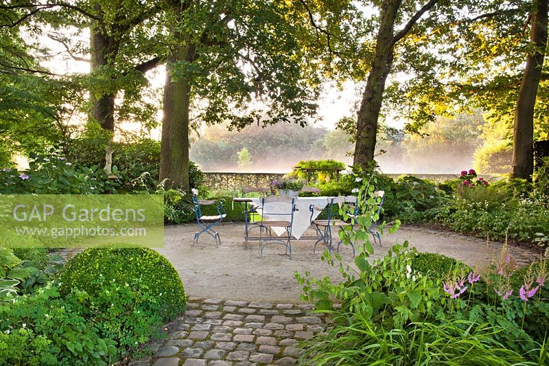 Garden set on circular gravel patio in wood area. Design: Dina Deferme