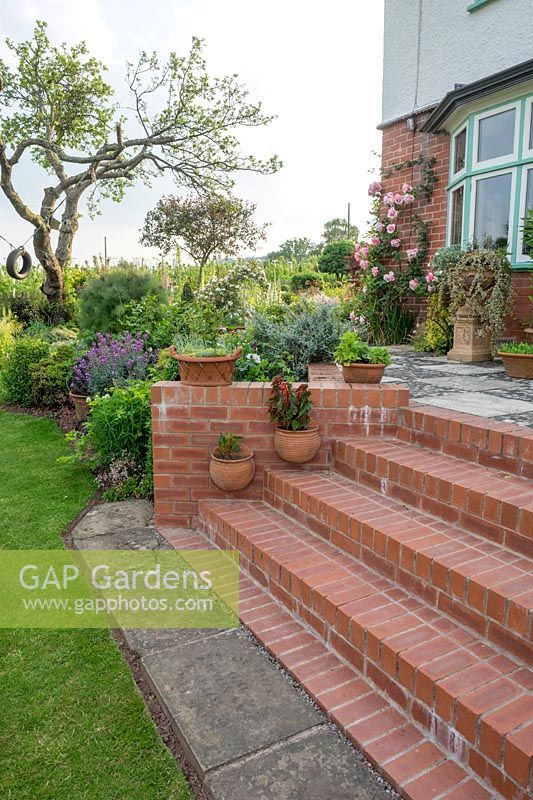 The brick steps from the crochet lawn to the patio are decorated with ceramic pots both freestanding and hung from the wall