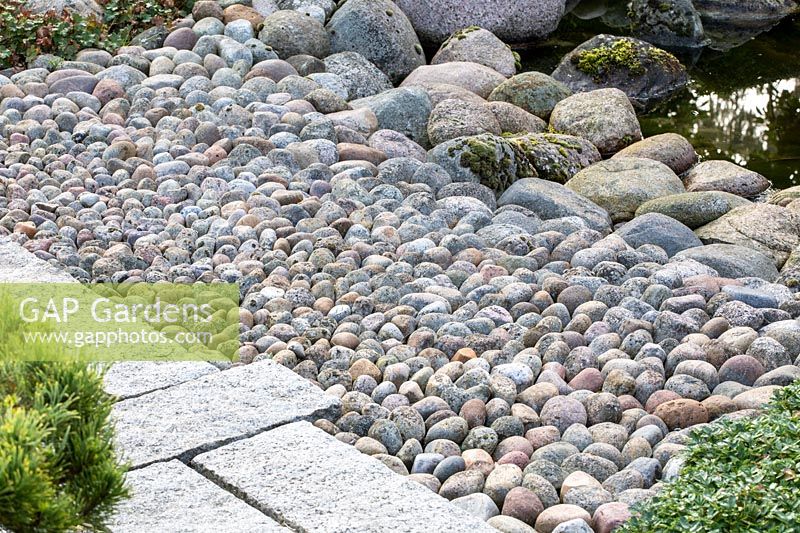 Details of the materials used in an Asian garden: densely stacked pebbles as transition from the boulders at the water edge to the flagstone paved garden path.