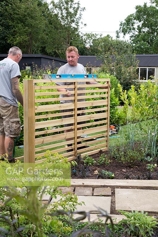 Men using spirit level to ensure post and fencing panel is straight