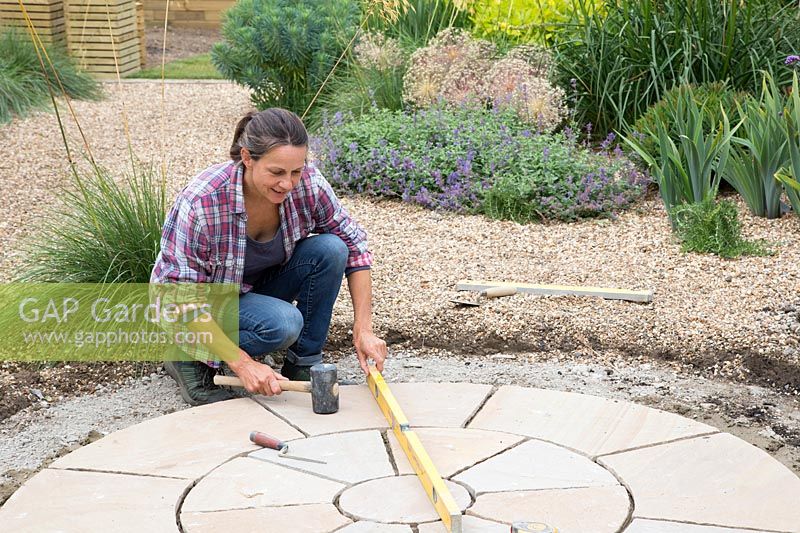 Woman using mallet to level paving slabs by checking spirit level