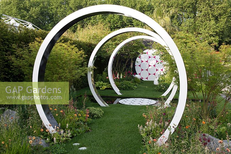 Breast Cancer Now Garden: Through the Microscope -Rings representing microscope lens with Acer trees and soft planting of Briza media, Geum 'Totally Tangerine', Gem 'Mai Tai' and Iris 'Natchez Trace' - RHS Chelsea Flower Show 2017
