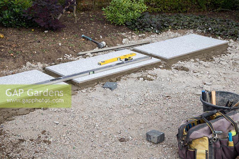 Making a mixed material patio - First row of large porcelain paving slabs laid on foundation of compressed finely crushed concrete