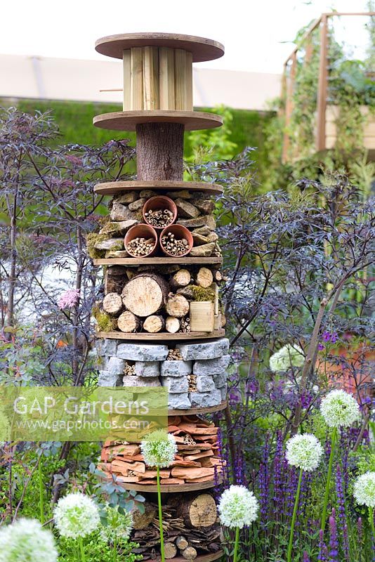 Insect house surrounded by white Allium balls in Greening Grey Britain Garden - RHS Chelsea Flower Show 2017 