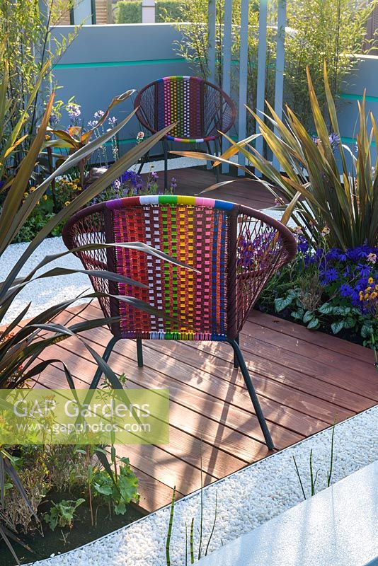 Colourful garden chairs with planting of bamboo, phormium and Pericallis x hybrida 'Senetti Deep Blue'- Ocean Garden, RHS Malvern Spring Festival 2017 